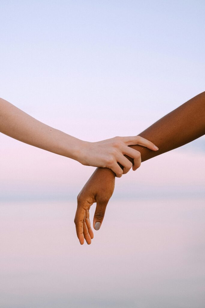 Close-up of two different skin toned hands holding gently against a serene sunset sky.